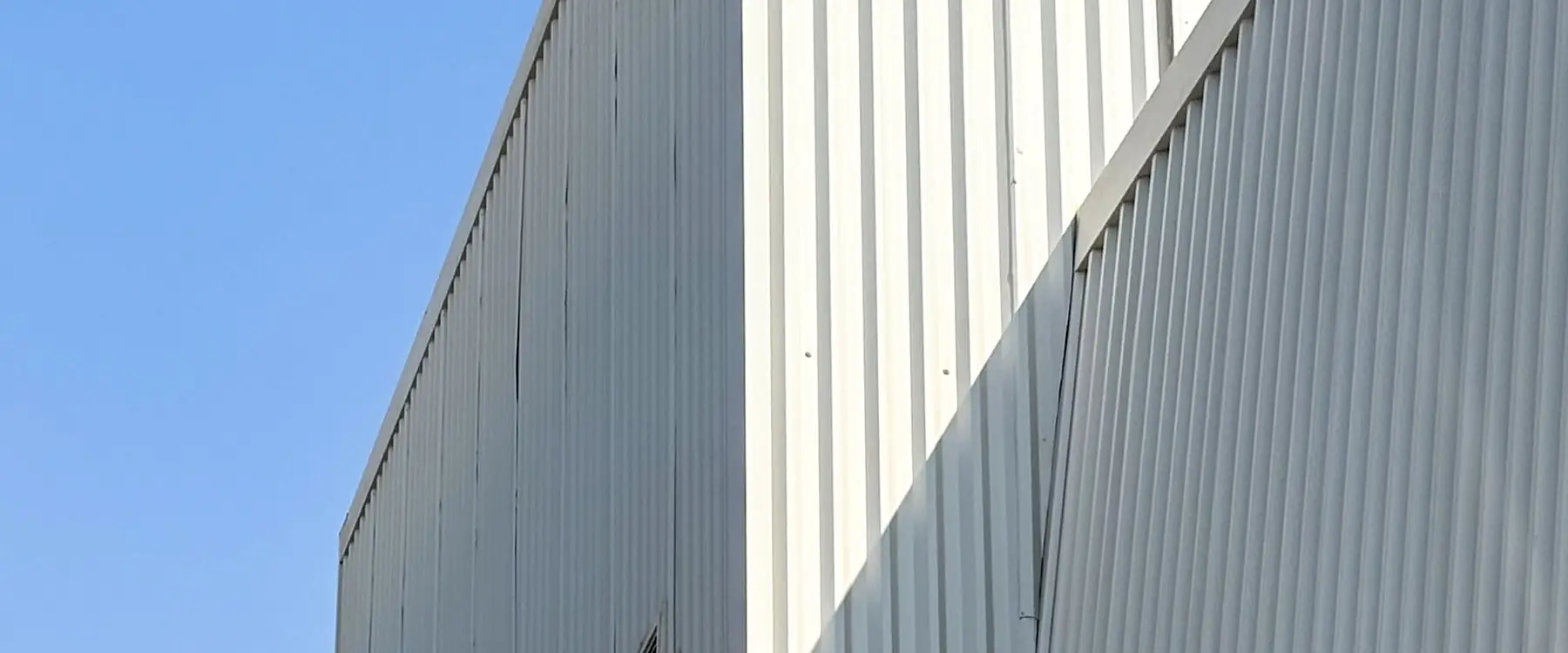 Corner of a large steel-clad building against a blue sky